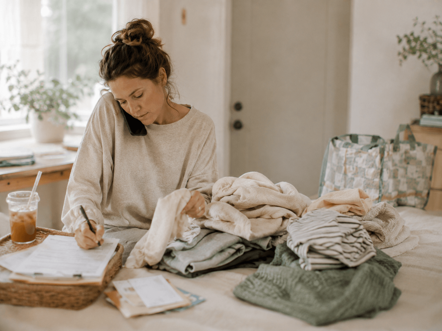 A woman on the phone sorting laundry and paperwork at home